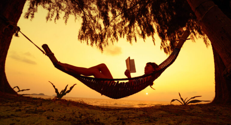 una donna che si surclassa su un'amaca mentre legge un libro al tramonto d'estate